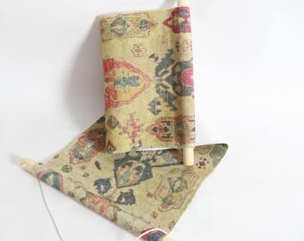 May include: Miniature rug with a traditional pattern in shades of yellow, red, and blue. The rug is rolled up on wooden dowels, with one end unrolled. The design features geometric shapes and floral motifs, ideal for dollhouses or miniature displays.