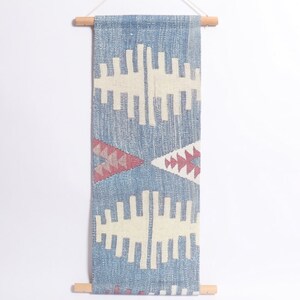 May include: A blue and white woven wall hanging with a geometric pattern. The hanging is attached to a wooden dowel rod.