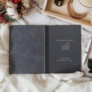 May include: A dark grey notebook with a white line pattern on the cover. The notebook is open to reveal a page with the text "Yes, I have the data." and a white line graph with an upward trend. The text "Melanie Smith, Applied Behaviour Analyst" is also printed on the page.