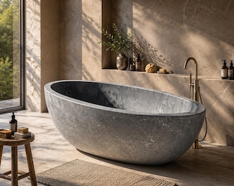 Puede incluir: Un baño moderno con una gran bañera ovalada de piedra gris. Un taburete de madera sostiene jabón y una botella. También se ven un grifo dorado y una cesta tejida. La habitación tiene una gran ventana con vistas a los árboles.