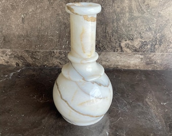 Puede incluir: Un jarrón de piedra de color blanco y crema con una base redondeada y un cuello alto y estrecho. La superficie presenta vetas marrones naturales en todo el material pulido, creando una apariencia suave y veteada con un borde ensanchado.
