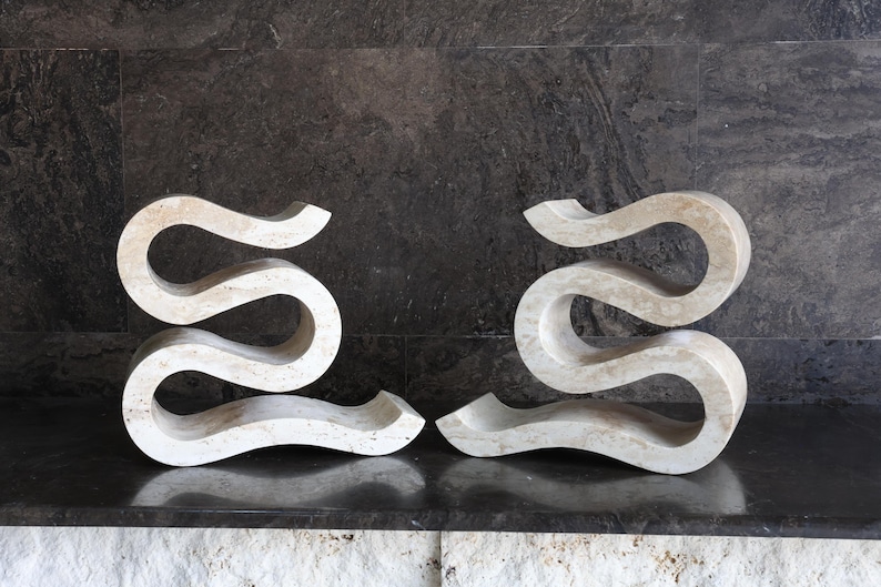 Puede incluir: Dos esculturas abstractas en color beige claro. Cada escultura tiene una forma serpentina fluida, con una base plana y una parte superior curva. Las esculturas est&aacute;n hechas de un material similar a la piedra y se exhiben sobre una superficie oscura.