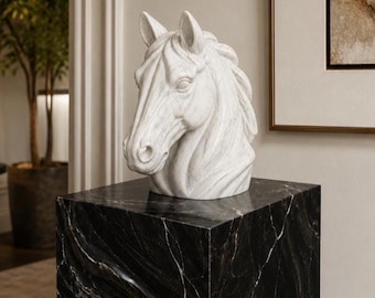 Puede incluir: Una escultura de cabeza de caballo de mármol blanco sobre un pedestal de mármol negro. La cabeza del caballo tiene detalles tallados y el pedestal tiene forma de cubo. Un elemento decorativo para el hogar.
