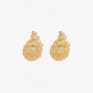 May include: A pair of gold-toned stud earrings shaped like spiral seashells. Each earring features a textured surface with horizontal ridges that mimic the natural growth patterns of a shell, creating a detailed and metallic finish.