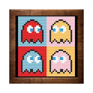 May include: A framed cross-stitch design featuring four Pac-Man ghosts in different colors: red, yellow, blue, and pink. Each ghost has a different colored background.