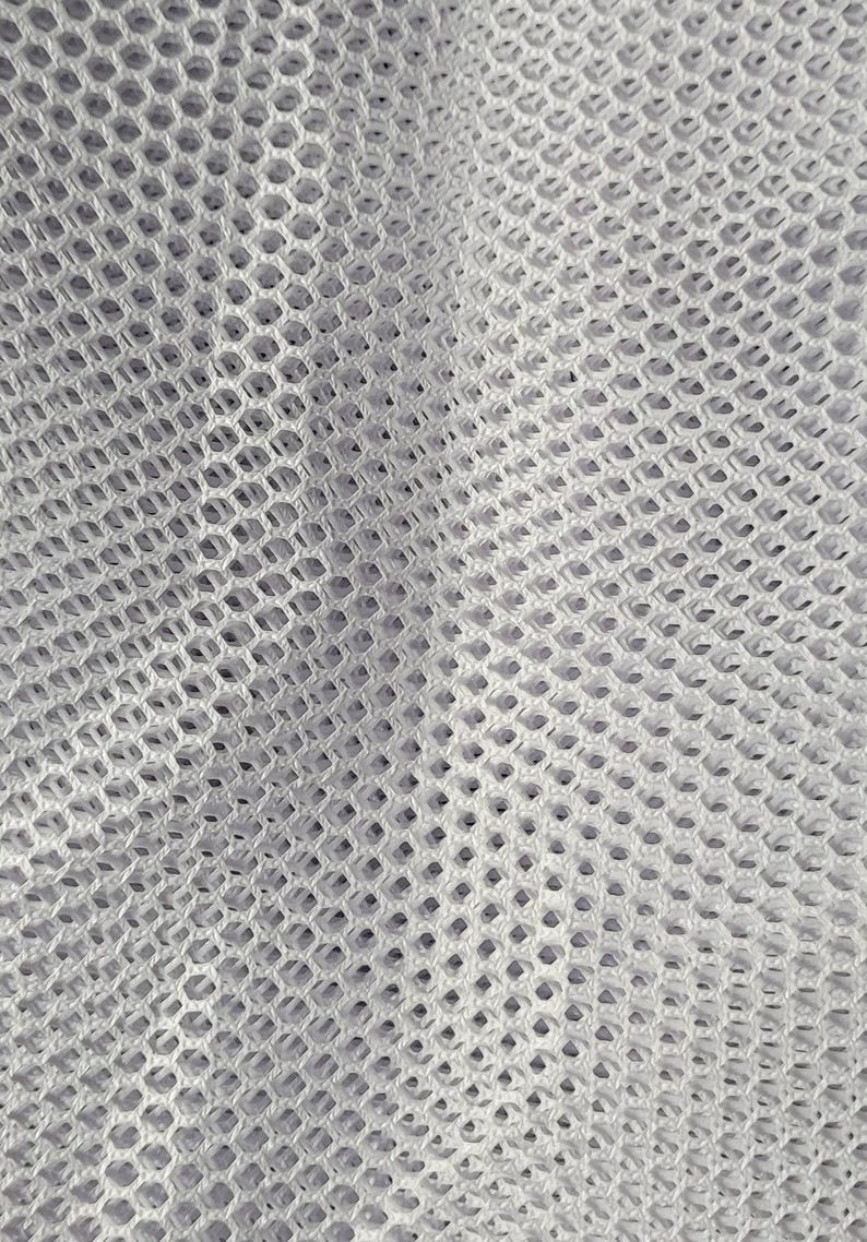 May include: Close-up of a white mesh fabric with a diamond pattern. The fabric is soft and flexible, and it has a slightly textured surface.