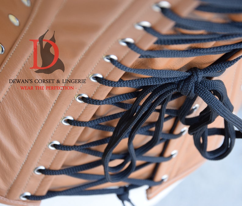 May include: A brown leather corset with black laces and silver eyelets. The corset is laced up the back and has a logo that says "Dewan's Corset & Lingerie - Wear the Perfection - "