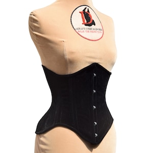 May include: Black velvet corset with silver metal eyelets and a hook and eye closure. The corset is on a mannequin.