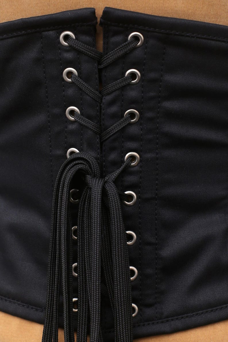 May include: Black corset with a lace-up back and silver eyelets. The corset has a satin finish and is tied with black cords.