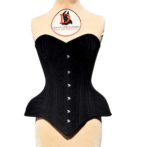 May include: A black velvet corset with a sweetheart neckline and a busk closure. The corset has a long line silhouette and is designed to cinch the waist. The corset is made by Dewan's Corset & Lingerie, which is printed on a label on the front of the corset.