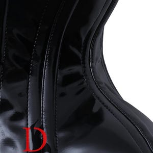 Puede incluir: Un cors&eacute; de charol negro con un logotipo D y el texto "DEWAN'S CORSET & LINGERIE - WEAR THE PERFECTION" en la parte delantera.