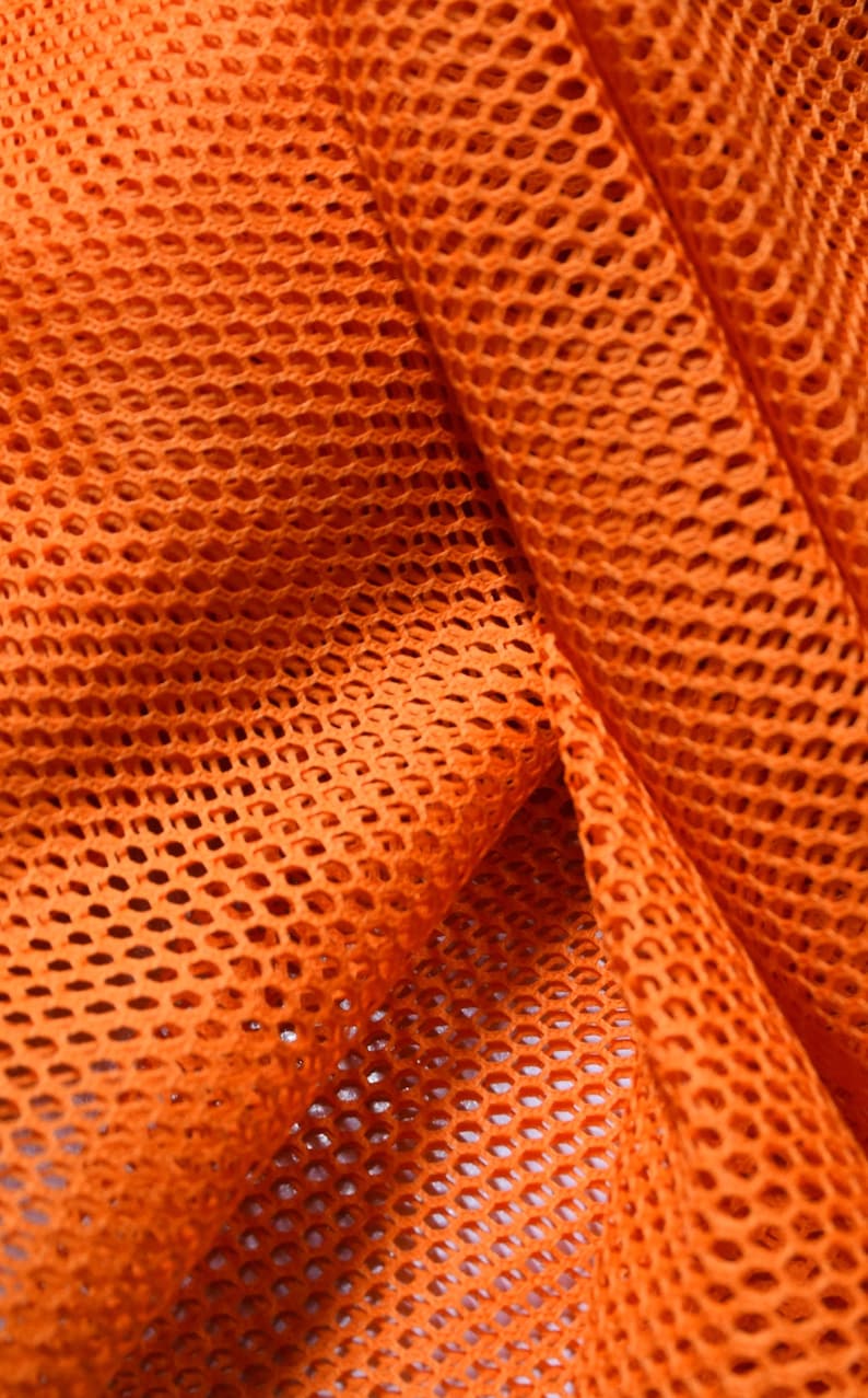 May include: Orange mesh fabric with a diamond pattern. The fabric is folded and shows the texture of the material.