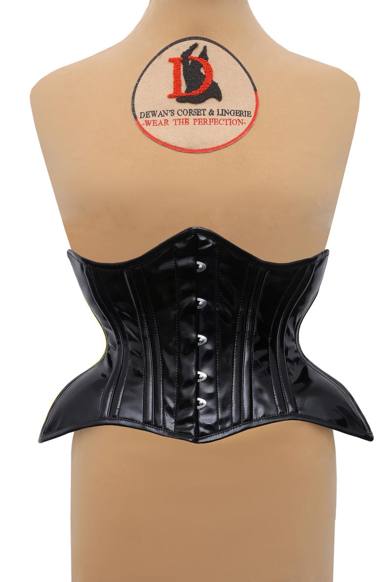 Puede incluir: Un cors&eacute; de charol negro con ribete amarillo y cierres de busk de metal plateado. El cors&eacute; tiene un dise&ntilde;o cl&aacute;sico con una cintura puntiaguda y una falda ancha y acampanada. El cors&eacute; se muestra en un maniqu&iacute;.