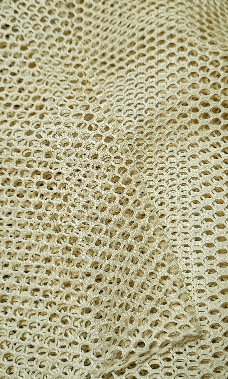 May include: Close-up of a beige mesh fabric with a woven pattern. The fabric is textured and has a slightly rough surface.