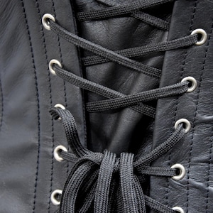 May include: Close-up of black leather with silver eyelets and black laces. The laces are tied in a knot at the bottom.