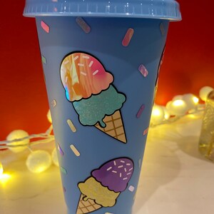 May include: A blue reusable cup with a lid and a straw. The cup has a design of ice cream cones with sprinkles on a blue background.