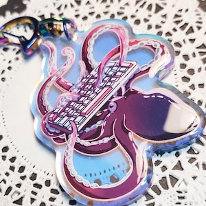 May include: A purple and blue iridescent octopus keychain with a white keyboard in its tentacles. The keychain is made of clear acrylic and has a silver metal ring.