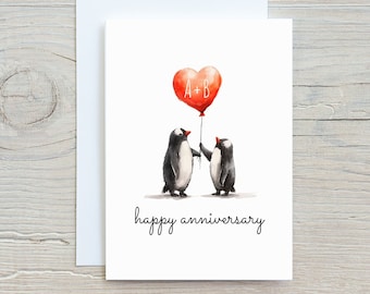 Op de afbeelding: Een witte wenskaart met een aquarel illustratie van twee pinguïns die een rode hartvormige ballon vasthouden met "A+B" erop. De woorden "happy anniversary" staan onder de pinguïns in een scriptlettertype.