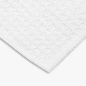 K&ouml;nnte beinhalten: Nahaufnahme eines wei&szlig;en, strukturierten Badetuchs. Das Handtuch hat ein gewebtes Muster und einen fertigen Rand. Die Ecke des Handtuchs ist sichtbar und zeigt die Dicke und Textur des Stoffes. Das Handtuch ist sauber und hell.
