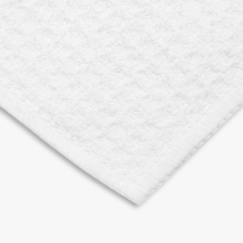 K&ouml;nnte beinhalten: Nahaufnahme eines wei&szlig;en, strukturierten Badetuchs. Das Handtuch hat ein gewebtes Muster und einen fertigen Rand. Die Ecke des Handtuchs ist sichtbar und zeigt die Dicke und Textur des Stoffes. Das Handtuch ist sauber und hell.