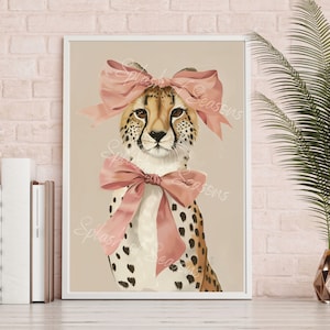 May include: A framed art print featuring a cheetah with a pink bow on its head and another around its neck. The cheetah has a tan and brown spotted coat, with brown eyes. The background is a neutral beige color.