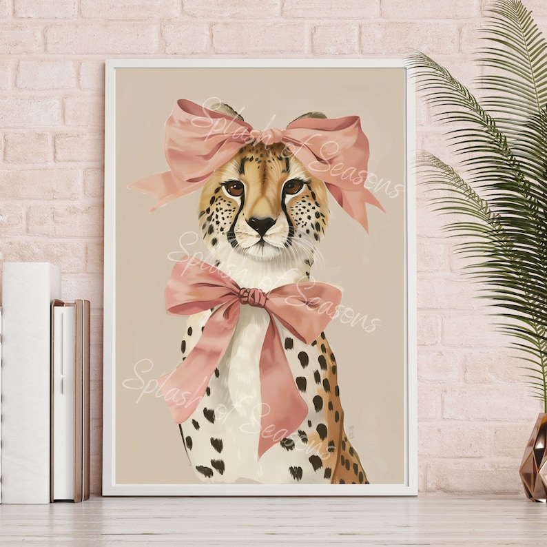 May include: A framed art print featuring a cheetah with a pink bow on its head and another around its neck. The cheetah has a tan and brown spotted coat, with brown eyes. The background is a neutral beige color.