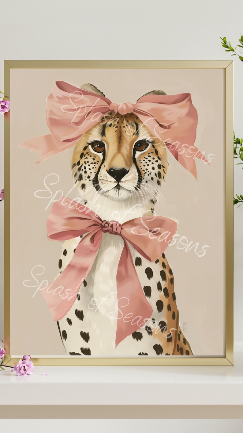 May include: Framed art print featuring a cheetah with a pink bow on its head and another around its neck. The cheetah has a tan coat with black spots and brown eyes. The background is a light beige color. The words "Splash of Seasons" are written across the image.