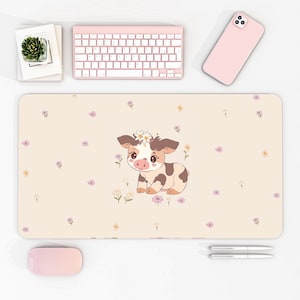 May include: A light brown and white cow with a pink nose and a daisy on its head is on a beige desk mat with a floral pattern. The mat is surrounded by a white surface with a pink keyboard, a pink phone, a pink mouse, and two silver pens.
