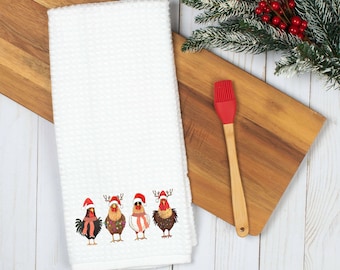 Pode incluir: Toalha de cozinha branca com um desenho bordado em vermelho, branco e verde de quatro galinhas usando chapéus de Papai Noel. As galinhas estão em pé em fila e têm penas de diferentes cores.