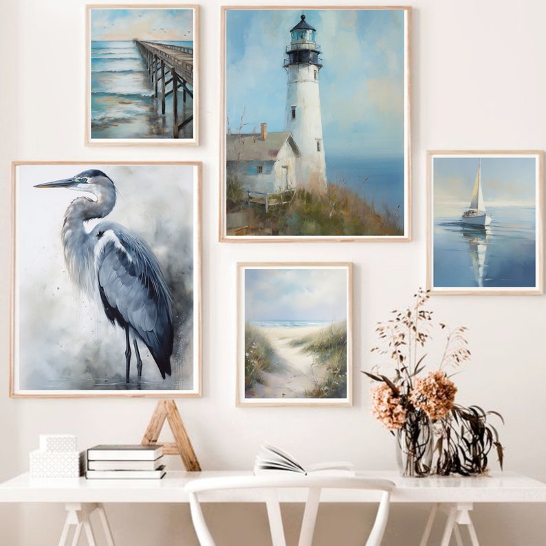 May include: Five framed watercolour paintings on a white wall above a white desk with a white chair. The paintings depict a lighthouse, a sailboat, a heron, a pier, and a beach path.