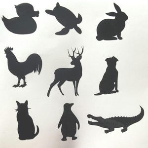 May include: Nine black silhouette cutouts of various animals are arranged on a white background. The animals include a duck, turtle, rabbit, rooster, deer, dog, cat, penguin, and alligator. Each cutout is a solid black shape.