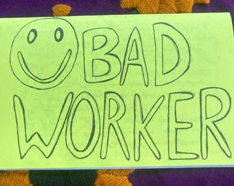 May include: A bright yellow card with black text that reads "BAD WORKER" and a black and white smiley face.