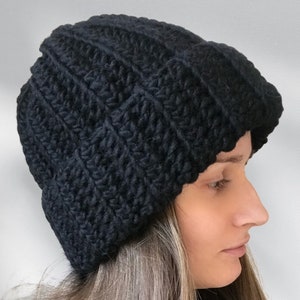 Könnte beinhalten: Eine schwarze Strickmütze mit Rippenstruktur. Die Mütze ist aus einem weichen, warmen Material gefertigt und perfekt für kaltes Wetter.