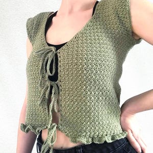 Peut inclure: Haut sans manches en crochet vert clair avec un col en V et une fermeture à nouer. Le haut présente un ourlet festonné et un motif de point texturé. Vêtement fait à la main.