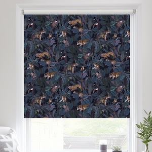 May include: A white armchair with a grey cushion sits in front of a window with a dark blue roller blind featuring a repeating pattern of leopards and foliage.