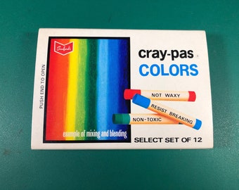 Op de afbeelding: Een doos Crayola Cray-Pas kleuren, een set van 12. De doos toont een regenboog van kleuren en de tekst "cray-pas COLORS" in blauw. De doos zegt ook "NOT WAXY", "RESIST BREAKING" en "NON-TOXIC".
