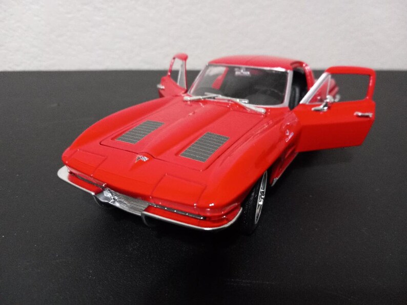 Puede incluir: Un coche modelo rojo Chevrolet Corvette de la d&eacute;cada de 1960 con las puertas abiertas. El coche tiene un parachoques cromado y una parrilla negra.
