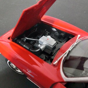 Puede incluir: Modelo de coche rojo de juguete con el cap&oacute; abierto, revelando un compartimento del motor detallado. El coche tiene un parabrisas negro y limpiaparabrisas plateados.