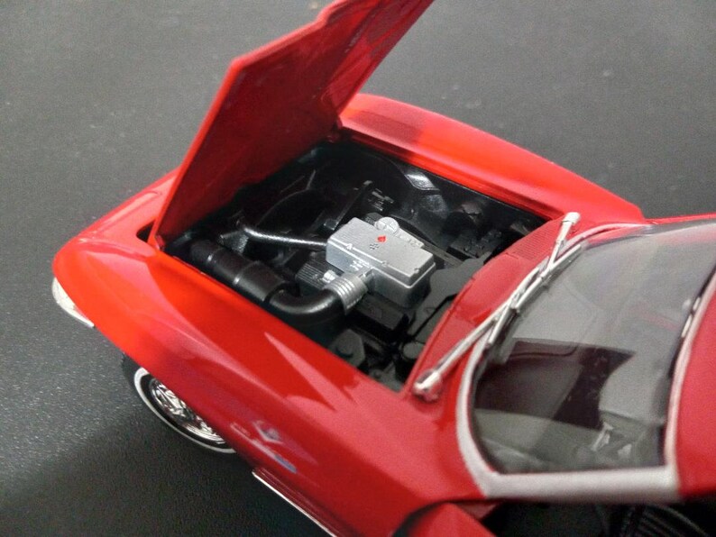 Puede incluir: Modelo de coche rojo de juguete con el cap&oacute; abierto, revelando un compartimento del motor detallado. El coche tiene un parabrisas negro y limpiaparabrisas plateados.