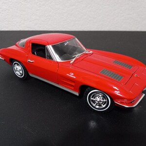 Puede incluir: Un coche modelo Chevrolet Corvette rojo de la d&eacute;cada de 1960 con interior negro y detalles cromados. El coche es un coup&eacute; con un cap&oacute; largo y una cubierta trasera corta. El coche est&aacute; sobre una superficie negra.