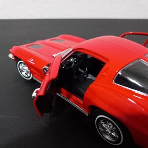 Puede incluir: Un coche modelo Corvette rojo de los a&ntilde;os 60 con la puerta del conductor abierta. El coche tiene ruedas cromadas y un interior negro.