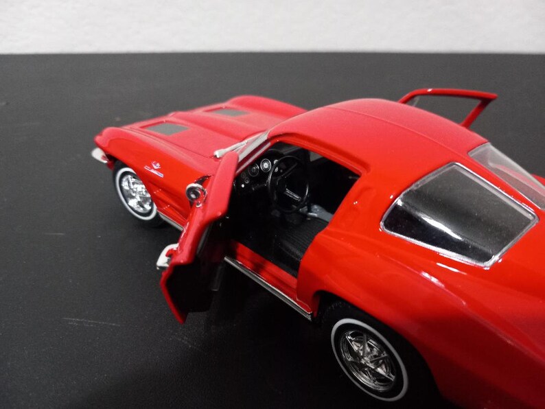 Puede incluir: Un coche modelo Corvette rojo de los a&ntilde;os 60 con la puerta del conductor abierta. El coche tiene ruedas cromadas y un interior negro.