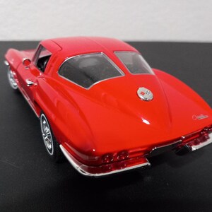 Puede incluir: Modelo de coche rojo Chevrolet Corvette Stingray 1963 con detalles cromados. El coche es un coup&eacute; con una ventana trasera y un emblema Corvette cromado en la parte trasera.
