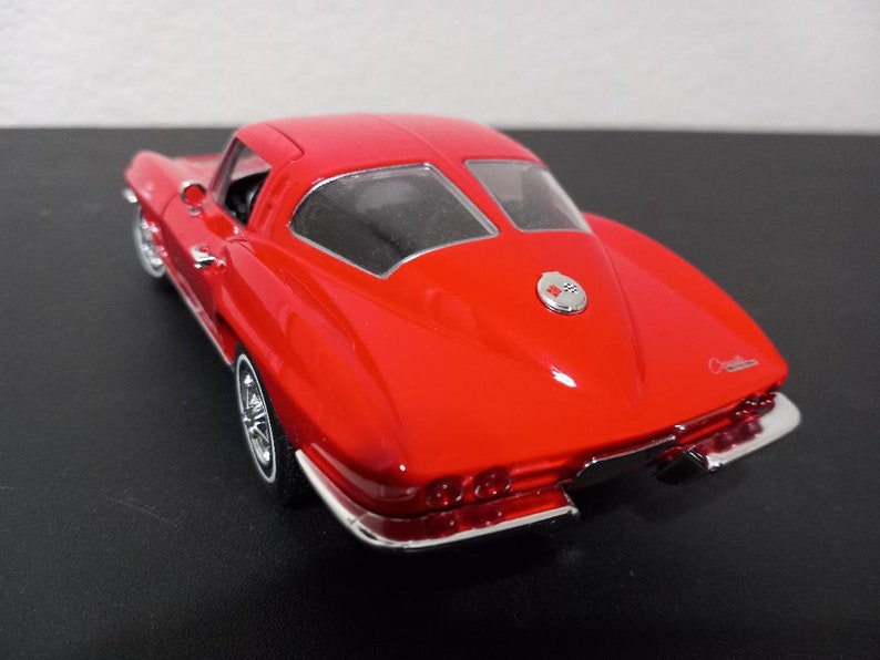 Puede incluir: Modelo de coche rojo Chevrolet Corvette Stingray 1963 con detalles cromados. El coche es un coup&eacute; con una ventana trasera y un emblema Corvette cromado en la parte trasera.