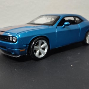 May include: A blue Dodge Challenger model car with a black stripe on the hood and silver wheels.