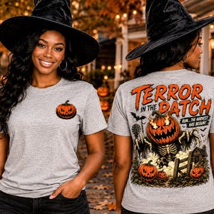 May include: A heather gray t-shirt featuring a small jack-o'-lantern graphic on the front left chest. The back displays a large, detailed illustration of a skeletal creature with a flaming pumpkin head, surrounded by pumpkins and the text TERROR IN THE DATCH RUN... THE HARVEST HAS BEGUN.