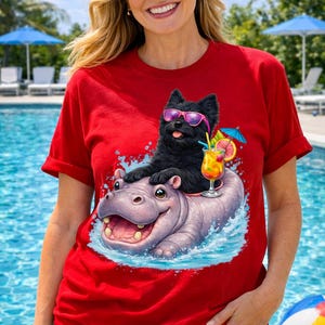 Pode incluir: Camiseta vermelha com uma ilustração de desenho animado de um cachorro preto usando óculos de sol rosa, montado em um hipopótamo na água. Um coquetel com um pequeno guarda-chuva está ao lado do cachorro. A camiseta está sendo usada por uma pessoa.