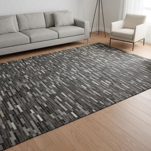 May include: A rectangular area rug featuring a patchwork design of small, elongated rectangular pieces in varying shades of charcoal, slate gray, silver, and white, arranged in a linear, brick-like pattern across the entire surface.