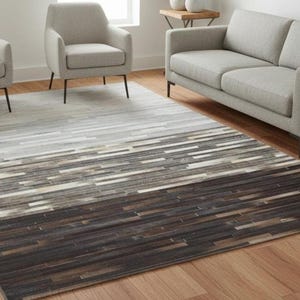 May include: A rectangular area rug with a gradient design, transitioning from light gray to dark brown. The rug features a pattern of horizontal, rectangular shapes, creating a textured appearance. The rug is placed on a hardwood floor.