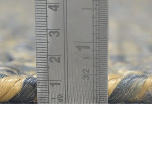 Puede incluir: Primer plano de una alfombra tejida con una mezcla de fibras azules y beige. La textura de la alfombra es visible, con una regla que muestra un grosor de aproximadamente 2,5 cm. La alfombra parece estar hecha de materiales naturales.